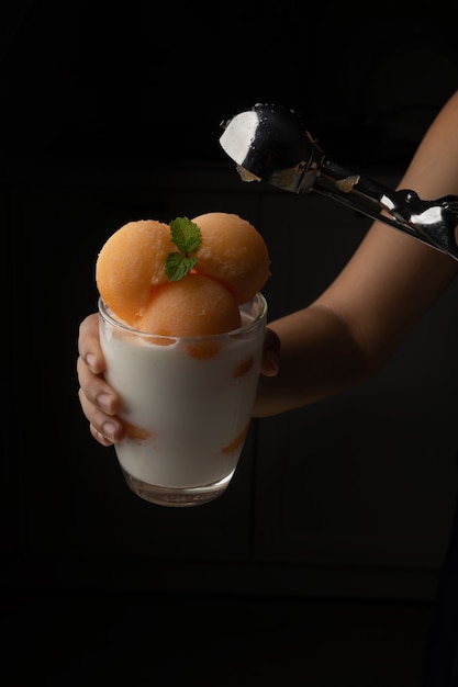 Foto il melone a polpa gialla è stato raccolto in una palla rotonda come il gelato messo in un bicchiere trasparente condito con latte fresco, dolce e delizioso. scatta una foto su uno sfondo nero