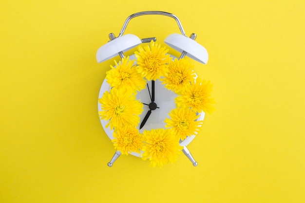 Photo yellow flowers on the dial of the white alarm clock in the center of the yellow surface