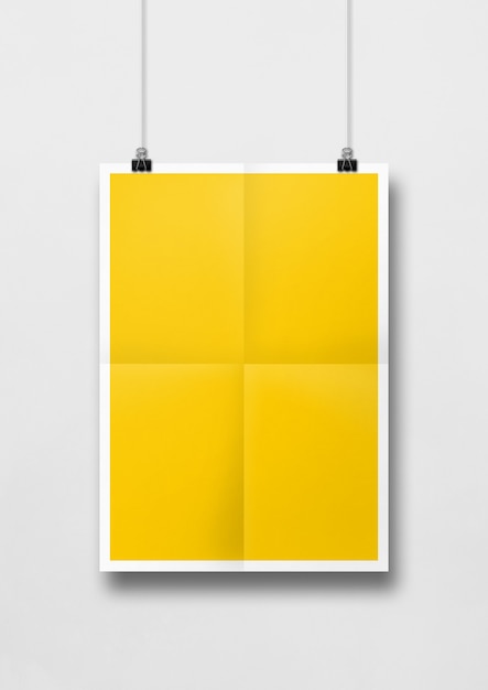 Yellow folded poster hanging on a white wall with clips.