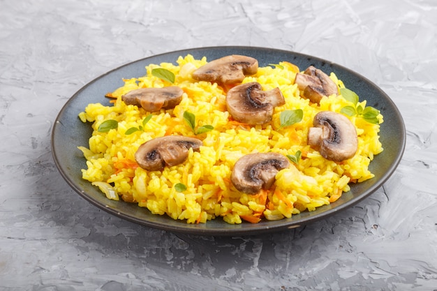 Yellow fried rice with champignons mushrooms turmeric and oregano on blue ceramic plate on a gray concrete background 