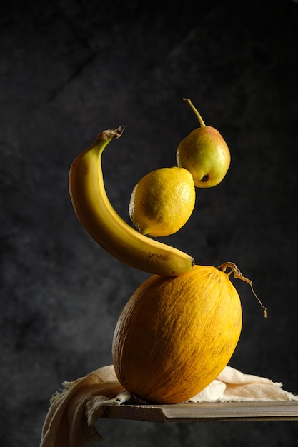 Yellow fruits on a black background, melon, banana, pear, lemon, on a wooden table, creative fruit