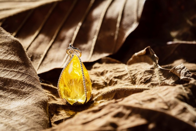 The yellow gemstone pendant with silver frame on leaf background.Vintage  pendant ,used for vintage fashion background