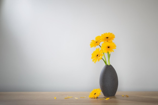 yellow gerbera in vase on wooden shelf