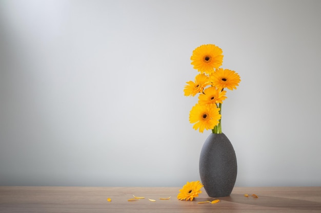 yellow gerbera in vase on wooden shelf