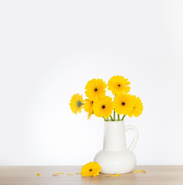 Photo yellow gerbera in white jug on wooden shelf on background wall