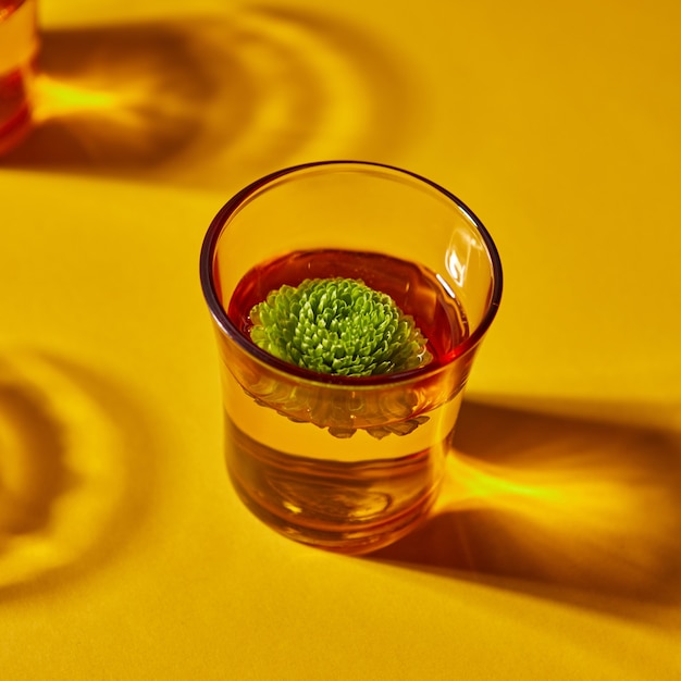 Yellow glass with beautiful deep shadows with water and a green bud flower on an orange background