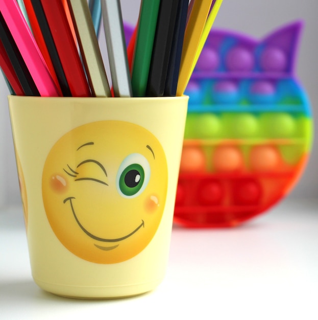 a yellow glass with colored pencils and a colorful antistress toy popit