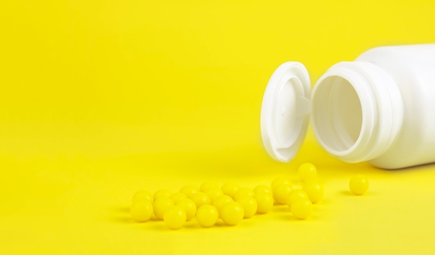 Yellow globules near white medical bottle, on a yellow background. vitamin c. medicine and healthcare