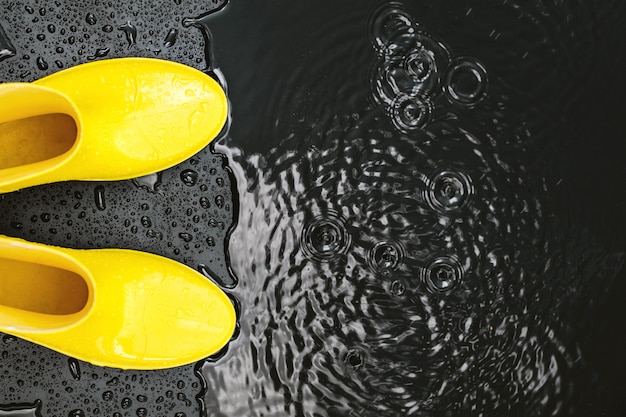 Yellow glossy gumboots stand in the rain on black 