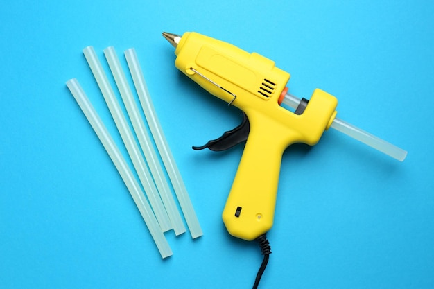 Yellow glue gun and sticks on light blue background flat lay