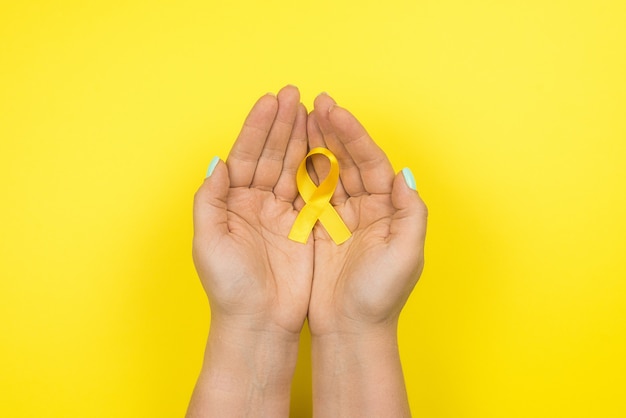 Yellow gold ribbon in the hands of a girl on yellow. 