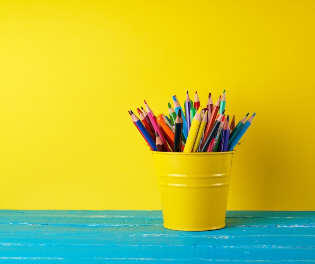 Yellow green bucket with multi colored wooden pencils and pens 