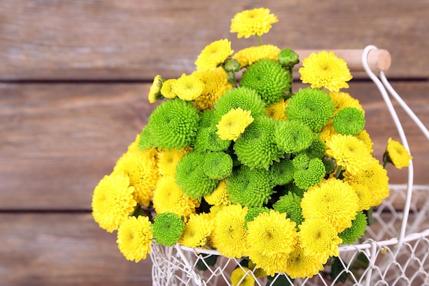 Yellow and green flowers in basket on wooden background