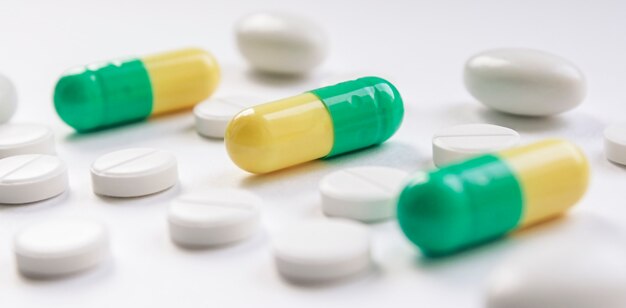 Yellow and green medical capsules and white pills on a white background