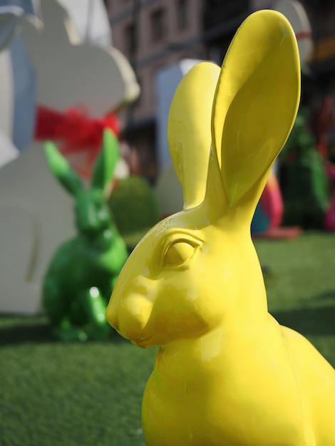 Yellow and Green rabbits sit in the grass in front of a white rabbit