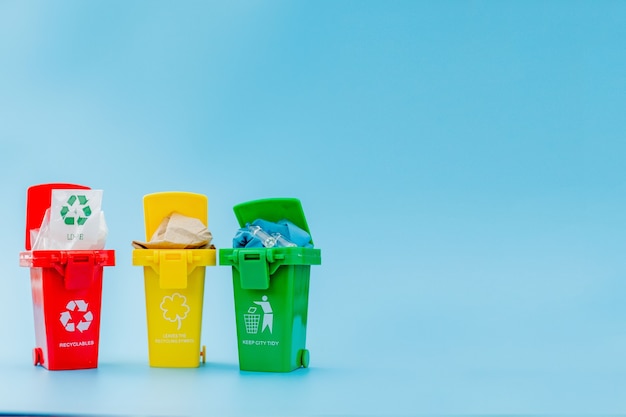 Yellow, green and red recycle bins with recycle symbol on blue background. Keep city tidy, Leaves the recycling symbol. Nature protection concept.