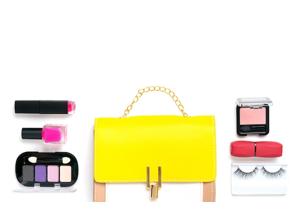 Yellow handbag with woman's accessories. Sunglasses, lipstick, blush, scrunchy, brushes isolated. Top view Flat lay