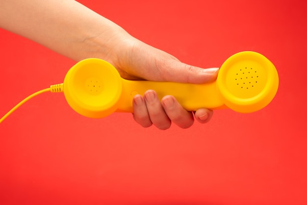 Желтая телефонная трубка на красной предпосылке в руке женщины.
