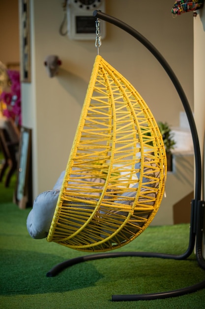 A yellow hanging chair with a round metal frame hangs from a green carpet.