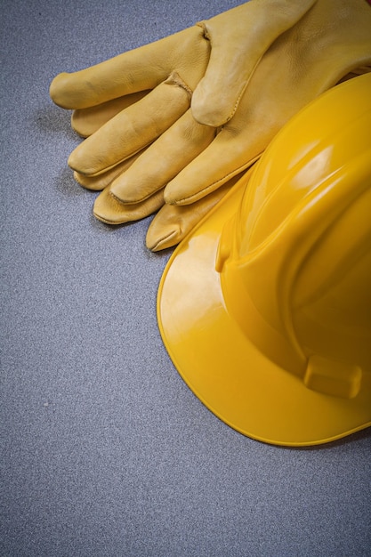 Yellow hard hat leather protective gloves on grey background construction concept