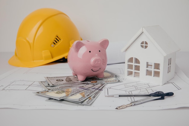 Yellow hard hat and piggy bank with drawings on engineer table