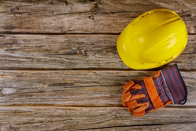 Yellow hard safety wear helmet hat in the construction site leather work gloves in a wood background