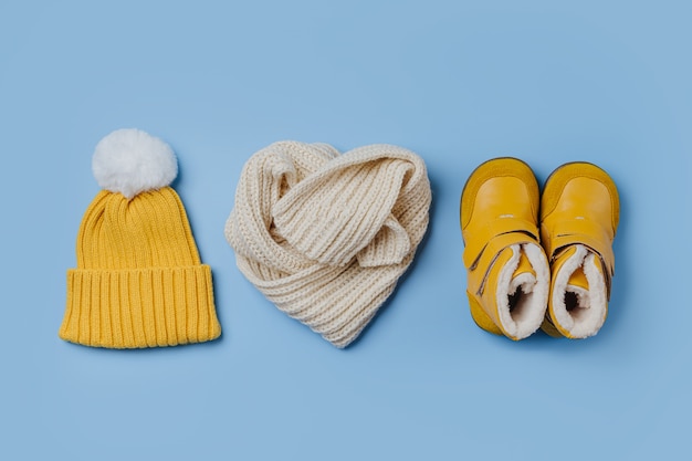 写真 黄色の帽子と青い背景にスカーフとブーツ。スタイリッシュな子供用アウター。冬のファッション衣装