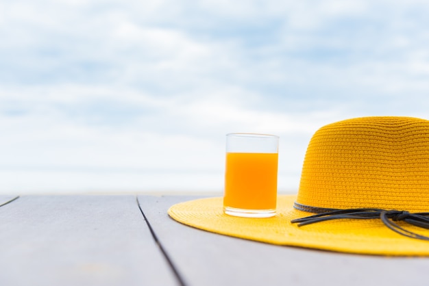 Yellow hat with fresh orange juice on the beach. Summer vacation with space on blue sky background.