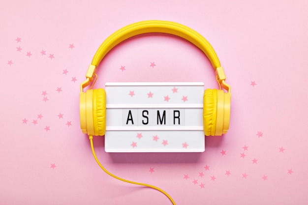 Yellow headphones ASMR letters lightbox and confetti on pink background ASMR Stressrelieving sounds concept flat lay