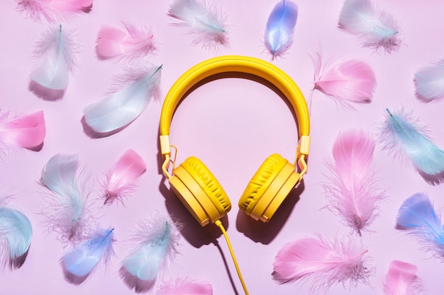 Yellow headphones and soft feathers on pink background ASMR Stressrelieving sounds concept flat lay trending shadows