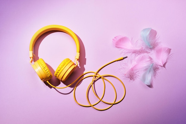 Yellow headphones and soft feathers on pink background ASMR Stressrelieving sounds concept flat lay trending shadows