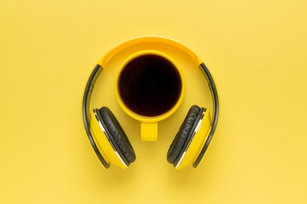 Yellow headphones and a yellow cup of coffee on a yellow background The concept of a stylish workplace