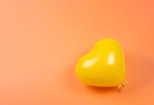 Yellow heart ballon on orange background. Copy space.