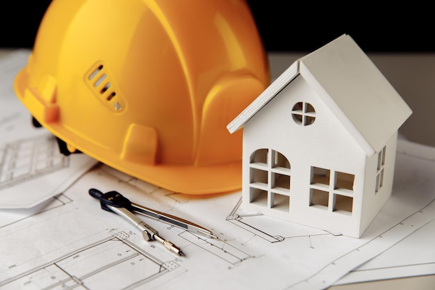 Foto casco giallo, mini casa e strumenti di disegno sui piani di costruzione.