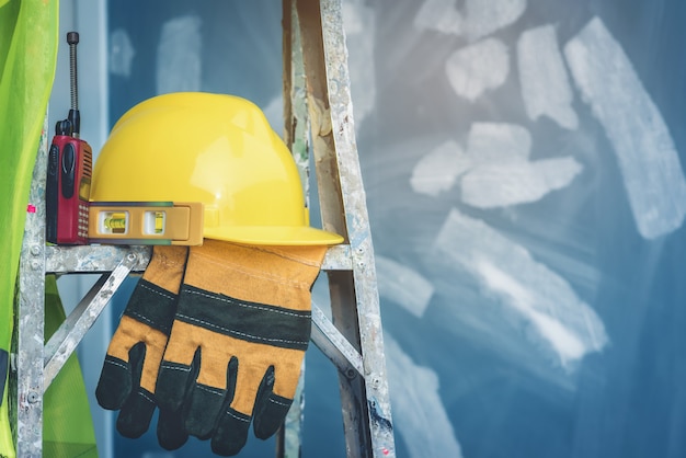 Photo yellow helmet with water level, gloves and radio that are placed on the folding ladder.