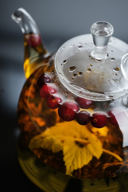 Yellow herbal tea in glass teapot and cup with leaves and berries Closeup   freshly brewed hot tea