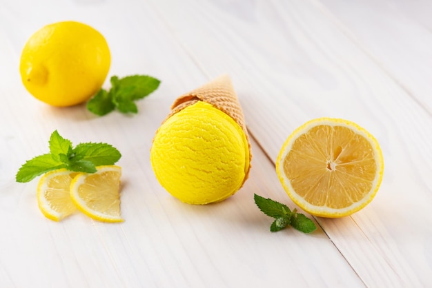 Yellow ice cream with lemon and mint in a waffle cone on a white wooden table
