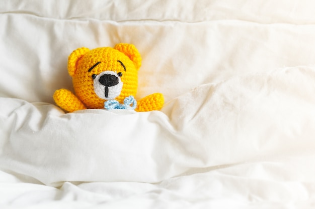 Yellow ill teddy bear lying in bed on white.