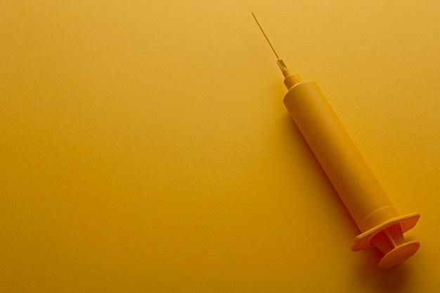 Yellow injection syringe on yellow background.