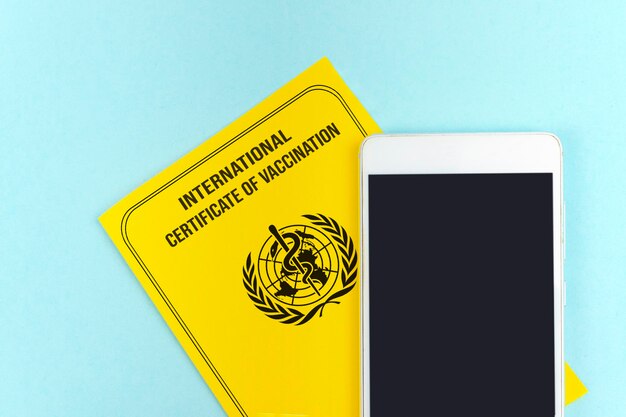 Yellow international certificate of vaccination with empty mock
up screen smart phone vaccine vial and syringe vaccination disease
immunity passport health and surveillance concepts