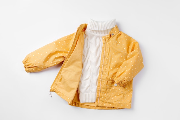 写真 白い背景の上の黄色いジャケットと暖かいセーター。秋の子供服のセットです。ファッションキッズ衣装。
