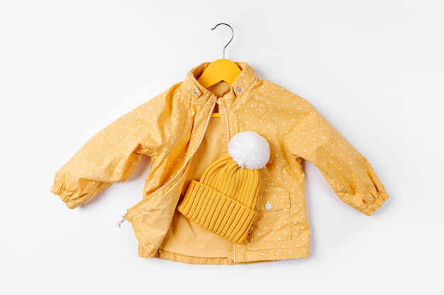 Photo yellow jacket hanging hanger with hat on white background. cute autumn kids outfit.