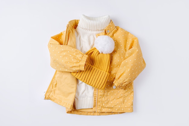 Yellow jacket and warm sweater and hat on white background. Set of children's clothes for autumn or winter. Fashion kids outfit.