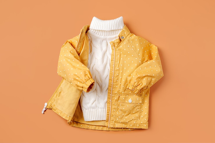 Photo yellow jacket and warm sweater on orange  background. set of children's clothes for autumn. fashion kids outfit.
