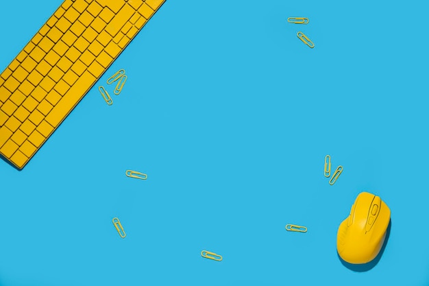 青色の背景に黄色のキーボード ワイヤレス コンピューター マウス ペーパー クリップ トップ ビュー フラット レイアウト