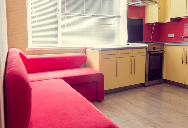 Yellow kitchen with cupboards, window, laminate and red soft couch