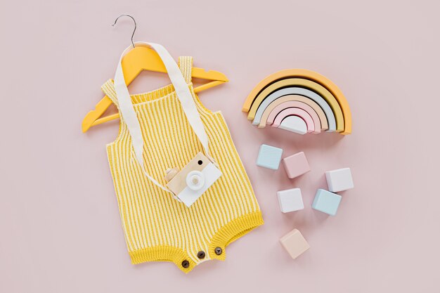 Yellow knitted romper  on hanger with toy camera and wooden toys. Set of baby clothes and accessories for spring or summer. Fashion childs outfit. Flat lay, top view