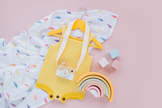 Yellow knitted romper  on hanger with toy camera and wooden toys. Set of baby clothes and accessories for spring or summer. Fashion childs outfit. Flat lay, top view