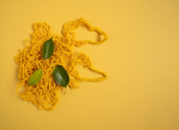 A yellow knitted string bag with green leaves lies on a yellow background The concept of zero waste replacement of plastic bags