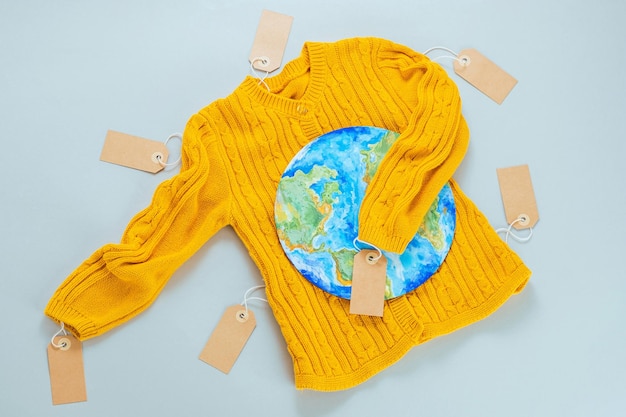 A yellow knitted sweater with a painted planet Earth on a gray background. Buy less.